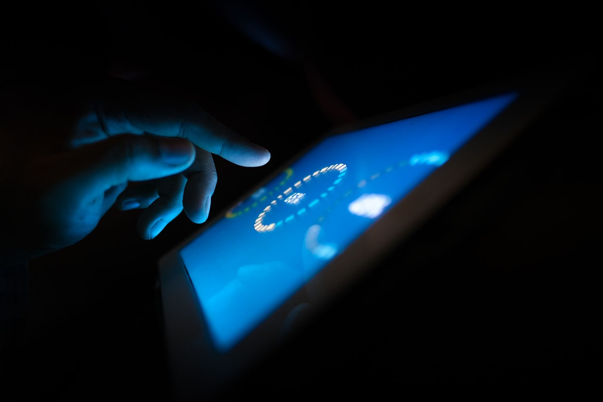 A hand touching a glowing tablet screen in the dark